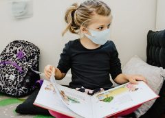 Young girl wearing a mask and reading a book in school