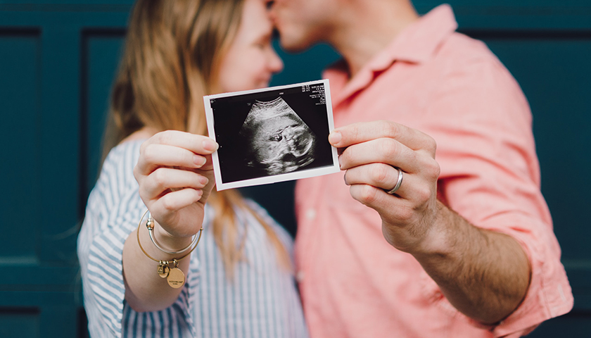 Couple kissing, holding up ultrasound in front of them