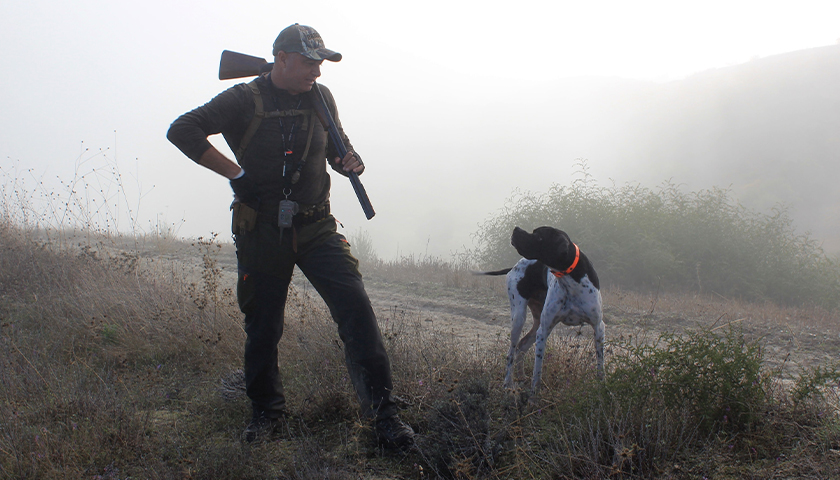 hunter standing next to his hunting dog at dusk